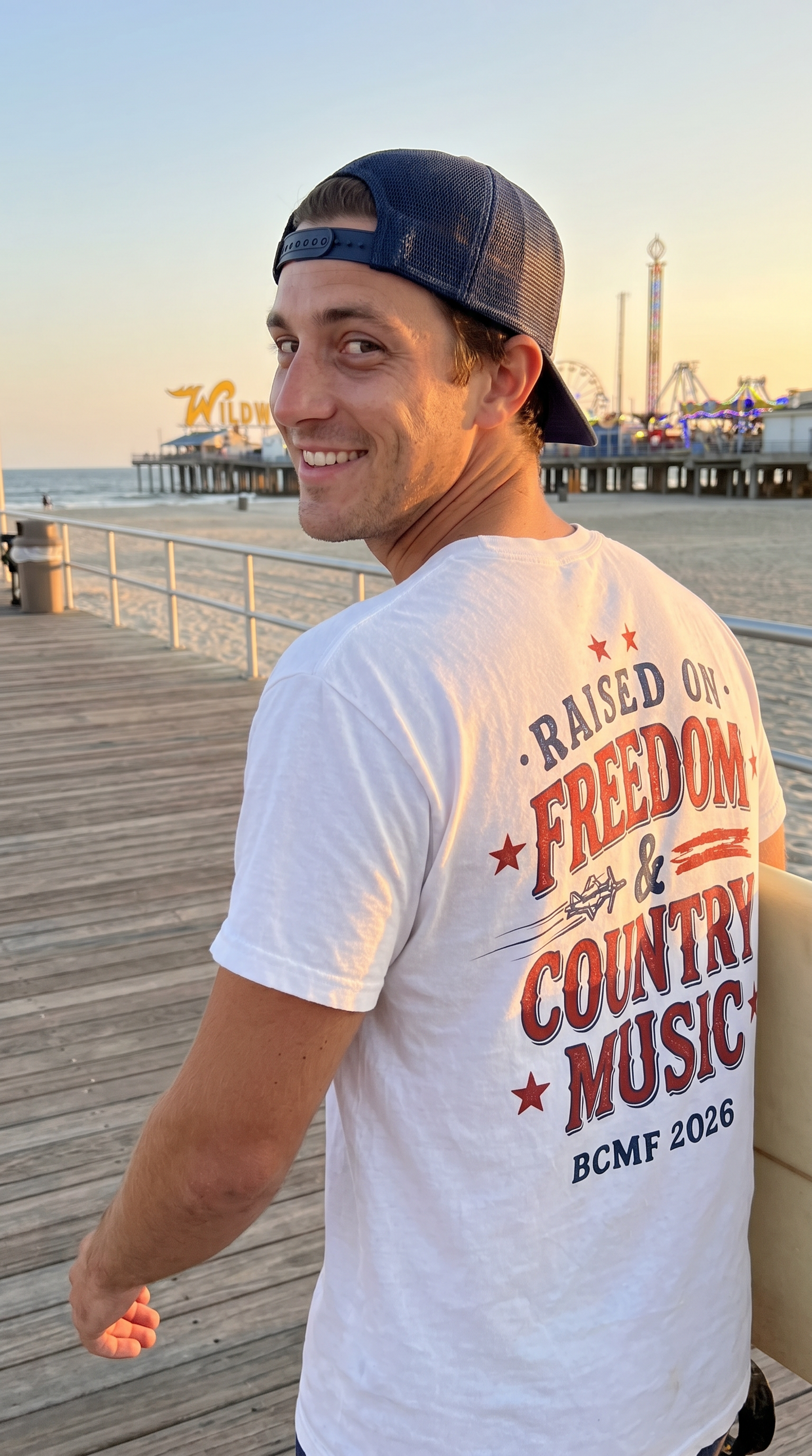 Man wearing white Raised on Freedom & Country Music back print tee on Wildwood boardwalk at golden hour